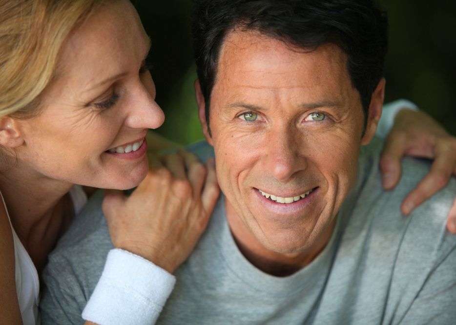 Woman leaning lovingly over smiling man's shoulder