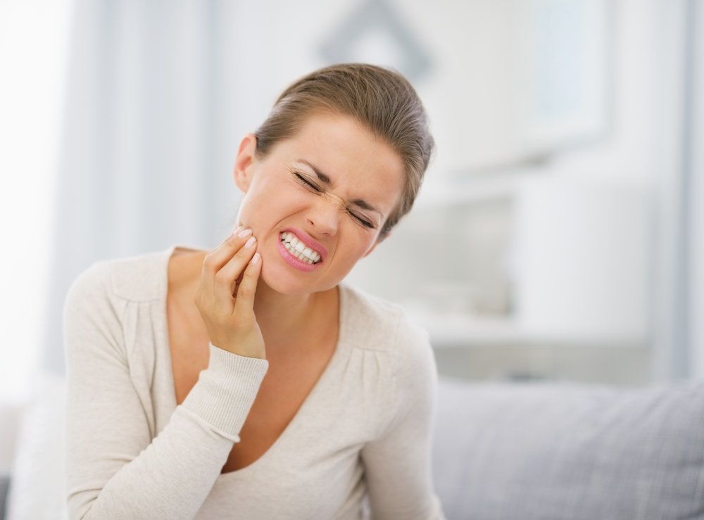 Grimacing young woman holding jaw in pain